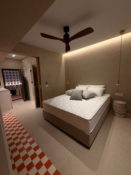 A double bed in warm evening light beneath a dark wooden ceiling fan