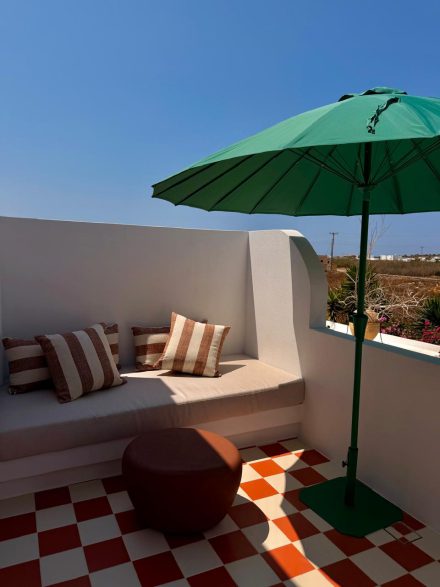 Terrace seating with striped cushions under a green parasol in full sun