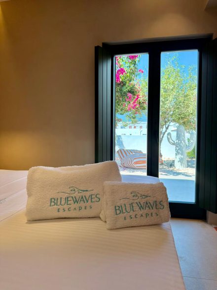 Two folded Bluewaves-branded towels on a made double bed, bougainvillea through the window